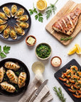Seafood Grill SeriosFood - masa cu fructe de mare la gratar: midii gratinate, file red snapper pe planseta, calamar tuburi in tigaie de fonta, frigarui creveti pe ardezie, salata goma wakame, vin alb, lamaie si ierburi pe fundal de beton alb
