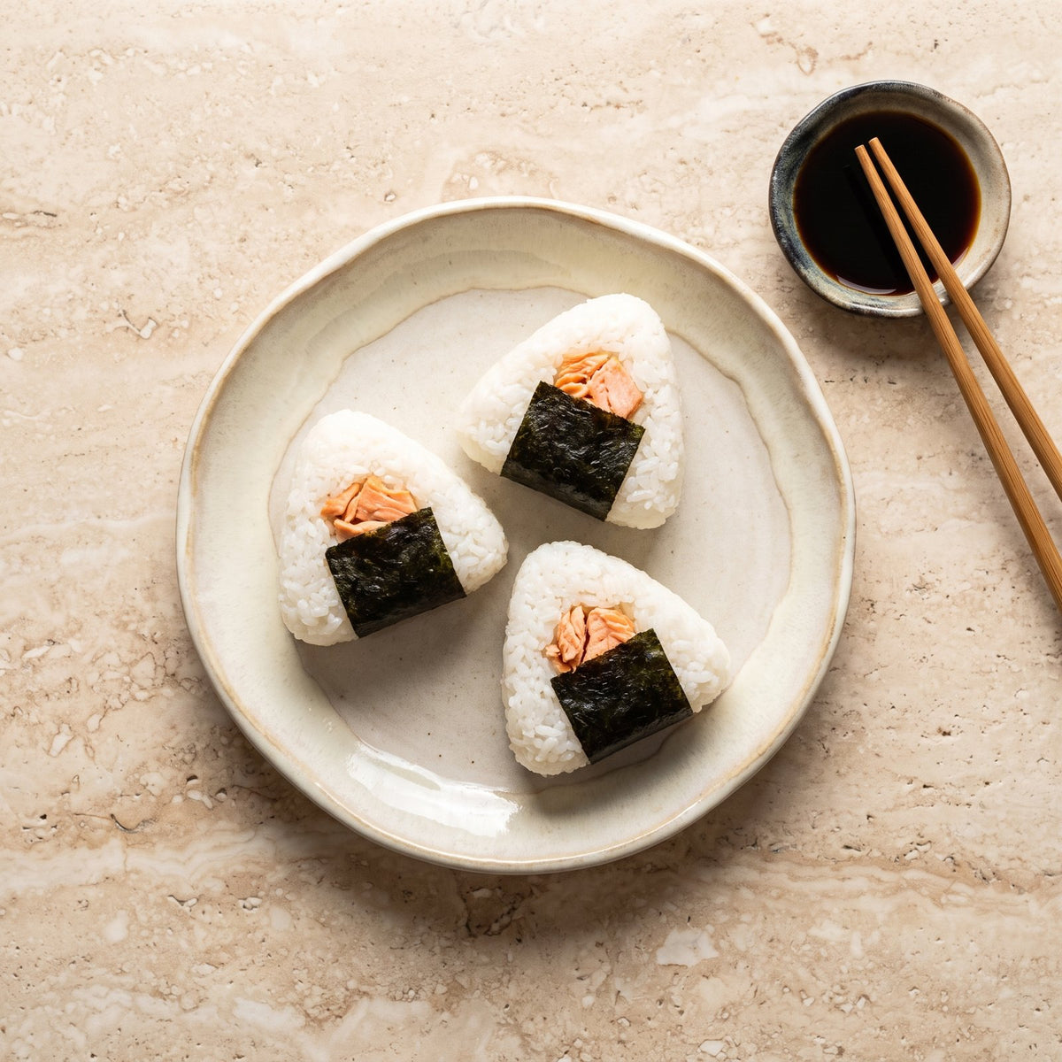Onigiri: trei triunghiuri de orez alb cu bandă de nori și umplutură de somon, pe farfurie ceramică