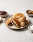 Deserturi asiatice pe farfurie cu ingrediente: dorayaki, hotteok, bile de susan, pastă de fasole adzuki, susan, făină de orez, miere