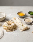 Tăiței asiatici și ingredientele lor: ramen, udon, vermicelli, foi de orez, făină, ou, orez crud pe blat de beton pal